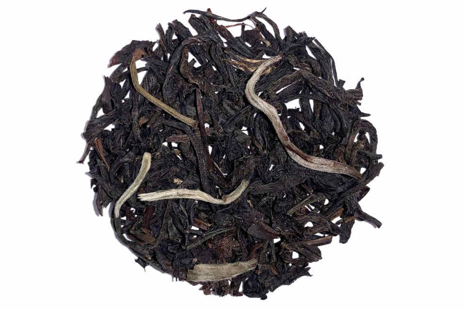 A close-up image of loose Smoky Earl Grey tea leaves, showing a mix of dark black and lighter silvery needles, indicative of the Silver Needle tea included in the blend.