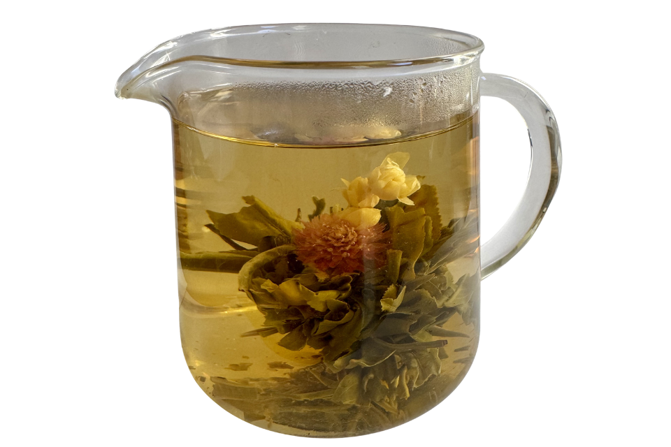 Clear glass teapot filled with floral tea on a white background