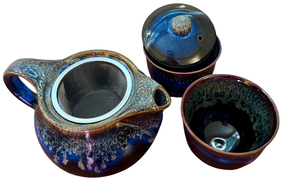 Ceramic teapot and two cups with a blue and brown speckled design on a white background.