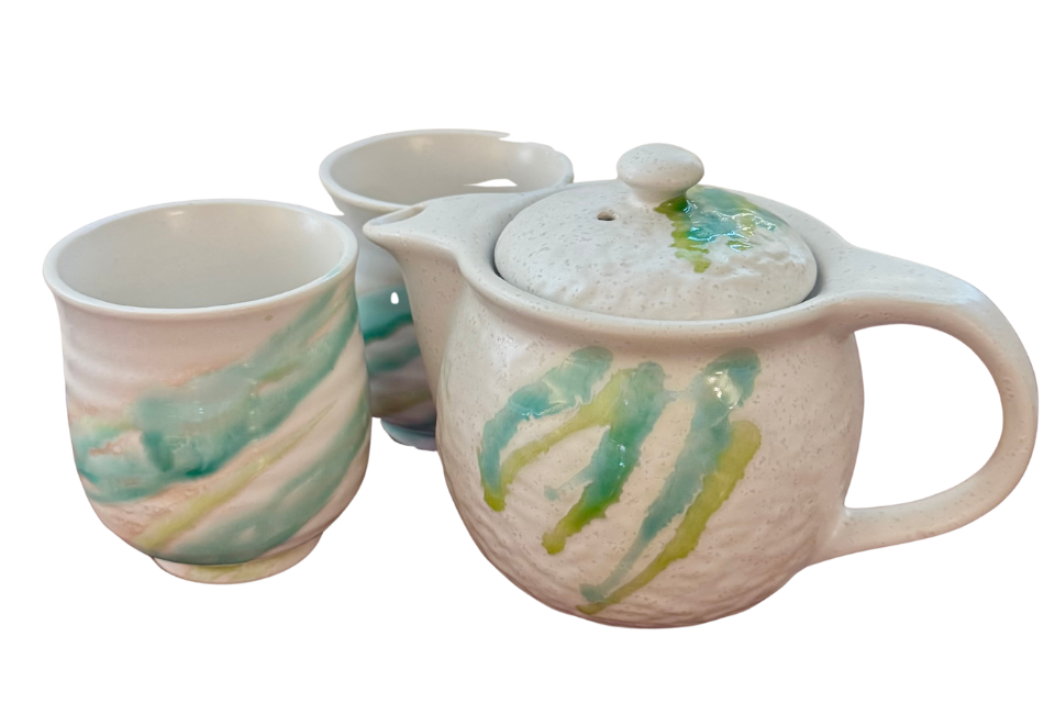 Ceramic teapot and mug set with green and yellow abstract designs on a white background