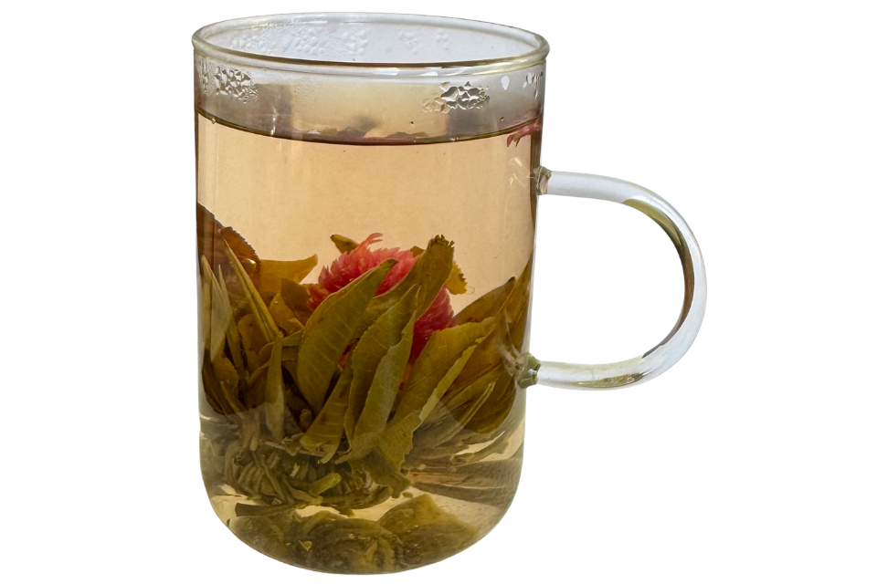 Clear glass mug with tea leaves and a pink flower on a white background