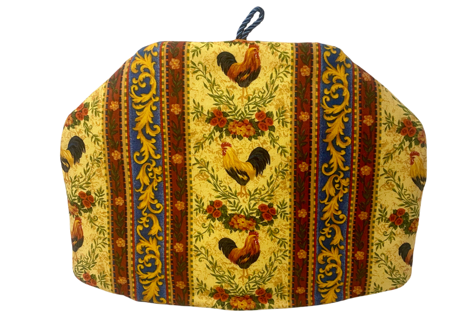 A multicolored tea cozy with a floral and rooster pattern on a yellow background, with a loop for hanging.