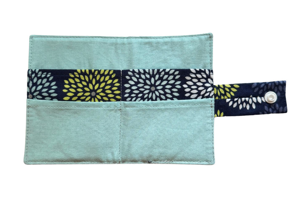 An open travel tea wallet with a pattern of blue sunburst and 4 compartments and a snap closure.