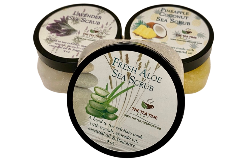 Three jars of handcrafted sea salt scrub, each with a different label indicating Fresh Aloe, Lavender, and Pineapple Coconut scents. The jars are closed and the packaging features green and purple botanical designs.