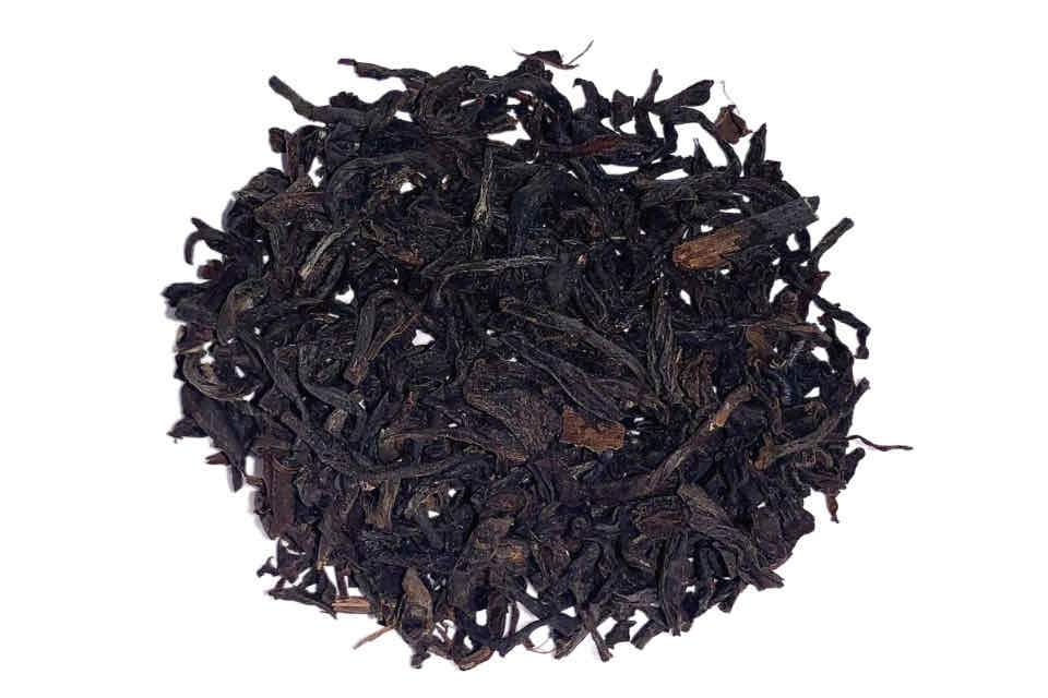 A heaping teaspoon of English Breakfast Black Tea on a white background, showcasing the tea's dark color and leafy texture.