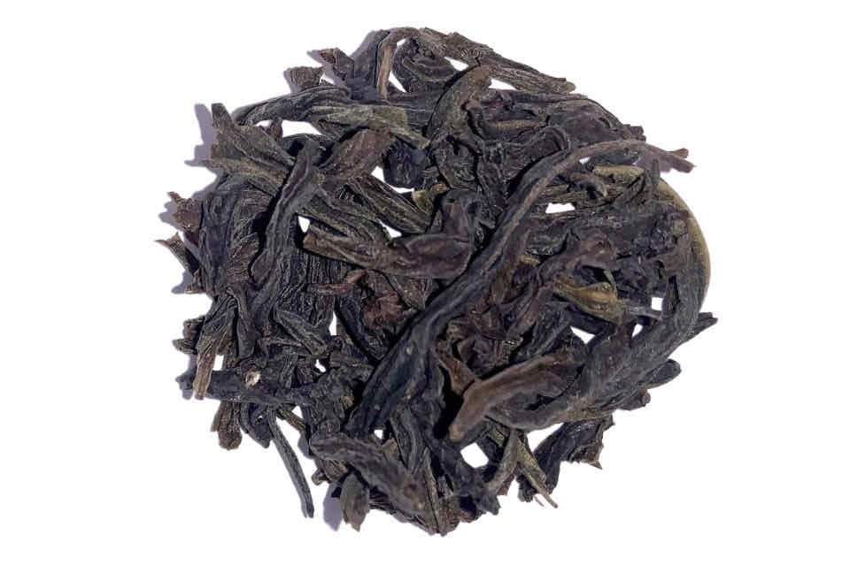 A pile of dry, twisted, dark green tea leaves.