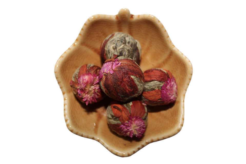 A hand-tied Guava Fruit Blooming Tea ball made with green tea and pink amaranth flower, displayed in a brown ceramic dish.