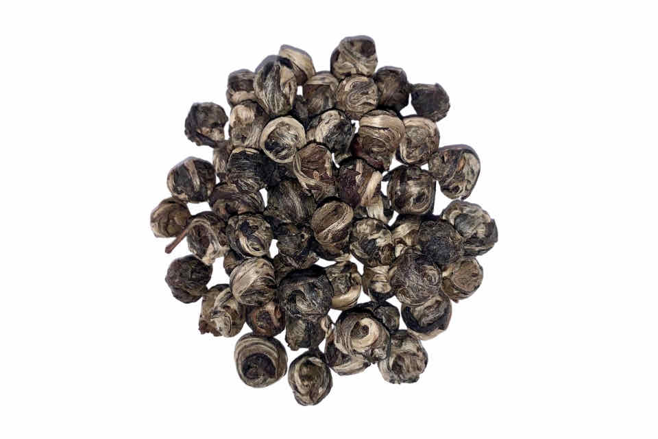 A pile of dried jasmine pearls tea leaves against a white background.