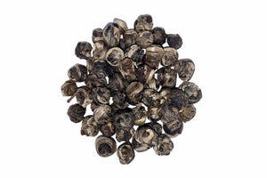 A pile of dried jasmine pearls tea leaves against a white background.