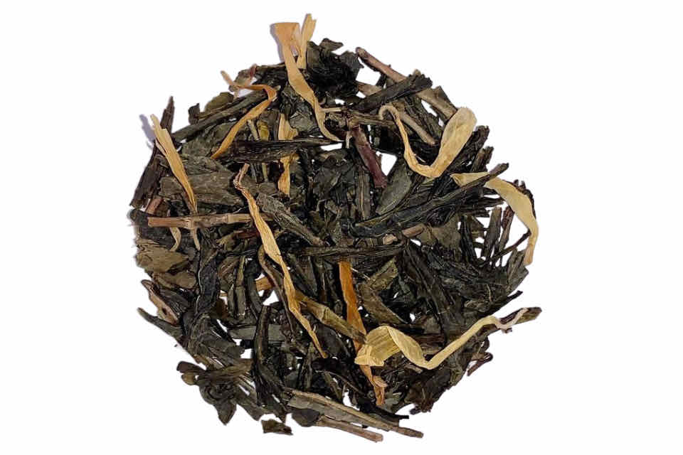 A close-up of dried tea leaves with pieces of pumpkin and vanilla, indicating a blend of green tea, marigold flowers, vanilla cream, and pumpkin flavor.