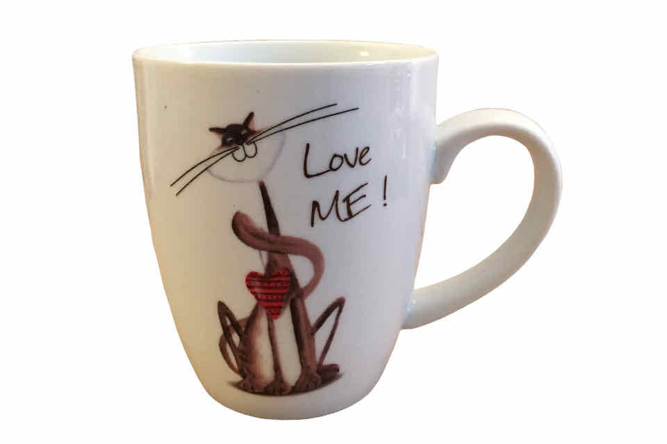 A white porcelain teacup with a hand painted cat and the words love me hand written next to the cat. 