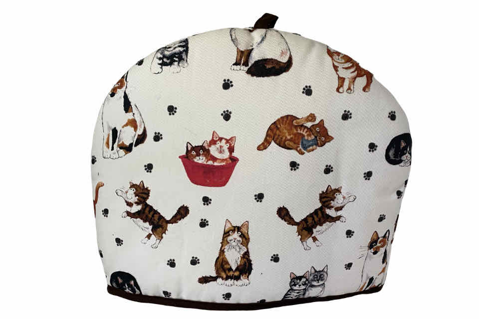 A fabric teapot cozy with a white background featuring various cartoon cats in different positions and a teapot illustration in the center.