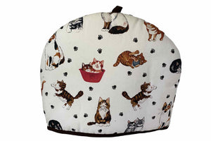 A fabric teapot cozy with a white background featuring various cartoon cats in different positions and a teapot illustration in the center.