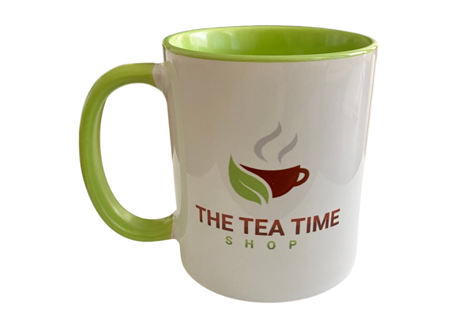 A white tea mug with a green hand a hand-painted logo The Tea Time Shop on the front. 