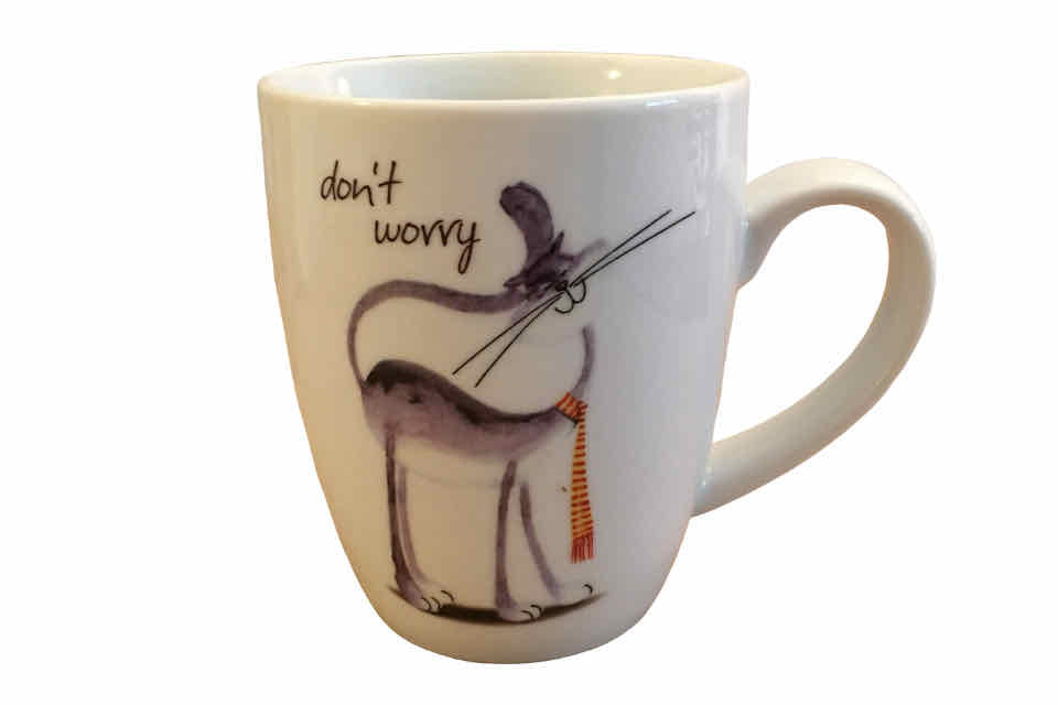 A white porcelain teacup with a cheerful cat and the words don't worry printed on it.