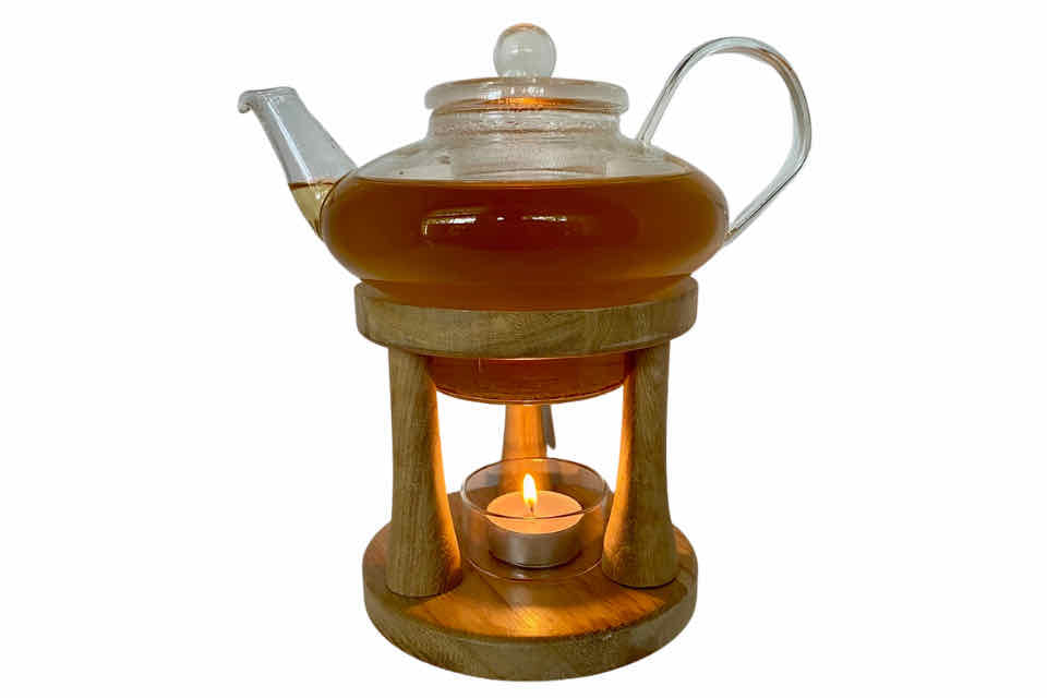 A glass teapot on a stand with a votive candle warmer