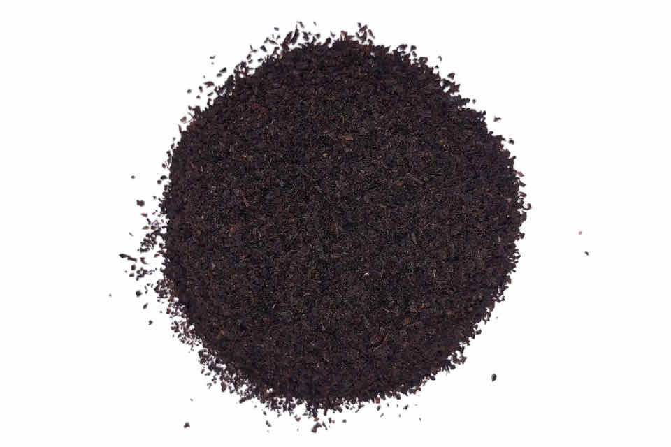 A pile of coarse black tea leaves with a vanilla cream appearance, indicative of the tea's flavor profile.
