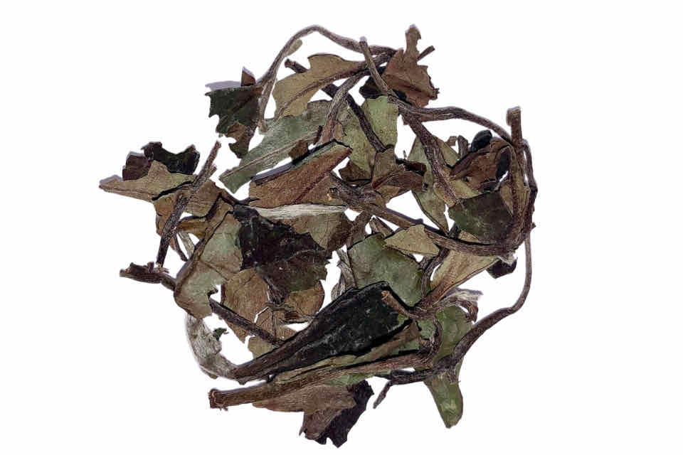 A pile of dried white peony tea leaves and buds against a white background.